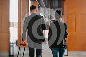 Business man and business woman talking and holding luggage traveling on a business trip, carrying fresh coffee in their