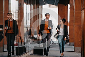 Business man and business woman talking and holding luggage traveling on a business trip, carrying fresh coffee in their