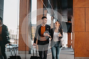 Business man and business woman talking and holding luggage traveling on a business trip, carrying fresh coffee in their