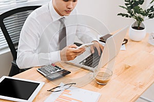 Business man busy working on laptop computer and using mobile smart phone in modern office, close up. Work process concept