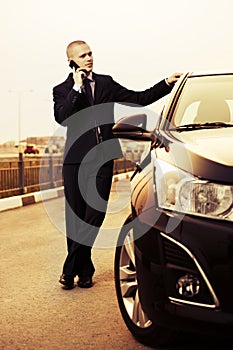 Business man calling on phone next to car