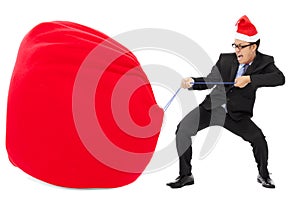 Business man carrying a heavy gift sack with christmas hat