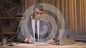 Business man checking and signing by pen contract. Boss in business suit sits at table in office. Signing on working