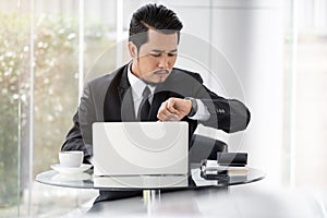 Business man checking time on smart watch while using laptop