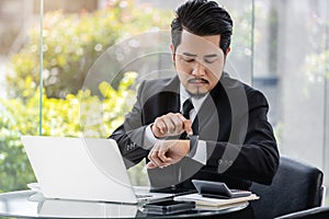 Business man checking time on smart watch while using laptop
