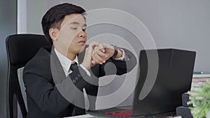 Business man checking time on watch while using laptop