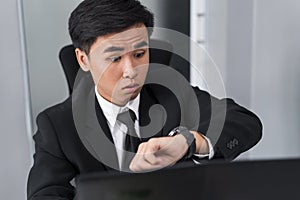 Business man checking time on watch while using laptop