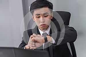 Business man checking time on watch while using laptop