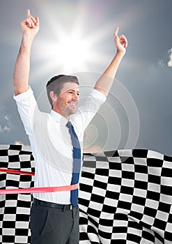 Business man cheering at finish line against sky and sun and checkered flag