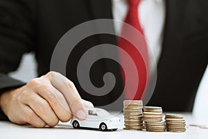 Business man and close up hand holding model of toy car red on over a lot money of stacked coins