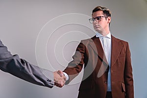 Business man closing a deal with another person. Two elegant men shaking hands. A man in a suit with a brown jacket