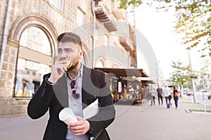 Business man with documents in his hands eats a snack while walking to work