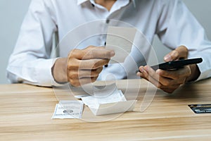 Business man entering password code on mobile phone paying bill with credit card bill on desk in home office