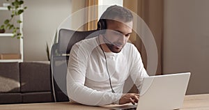 Business man freelancer agent call manager wears headphones head microphone looks into laptop screen typing on computer