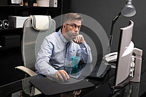 Business man with glasses working in the office at computer table and drinking coffee from bright Cup
