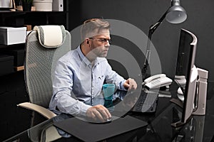 Business man with glasses working in office at computer table and drinking coffee from bright Cup