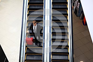 Business man going down escalator holding travel bag.