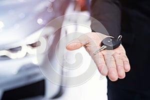 Business man hand holding car key front with car in showroom on background. transport dealership and sales concept.
