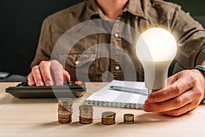 Business man hand holding a light bulb using a calculator to calculate cash flow. The idea of saving energy and accounting Finance