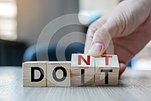 Business man hand holding wooden cube with flip over block DON T to DO IT word on table background. success, strategy, solution,