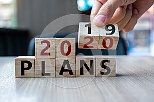 Business man hand holding wooden cube with flip over block 2019 to 2020 Plans word on table background. Resolution, strategy,