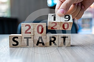 Business man hand holding wooden cube with flip over block 2019 to 2020 Start word on table background. Resolution, strategy,