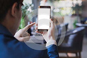 Business man hands holding blank screen smartphone in the coffee cafe. Mockup smartphone on male hands empty display with the blur