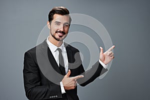 Business man has his hands up pointing his finger and smiling with his teeth open mouth in a business suit on a gray