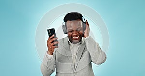 Business man, headphones and dance in studio with phone for celebration, freedom and winning on blue background. Happy