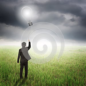 Business man holding bulb balloon in fields and raincloud