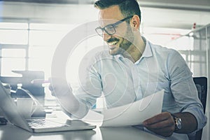 Business man holding document and checking e mail on laptop.