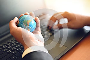 Business man holding earth globe model in hand and use a laptop - Business technology global and around the world concept