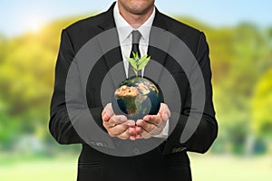 Business man holding earth with a plant growing on the top of the globe in his hands