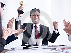 Business man holding a gold trophy. Happy and successful business team rewarded for in the office