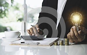 Business man holding light bulb on desk in office and putting calculator with coins or money on work desk also for idea,energy,