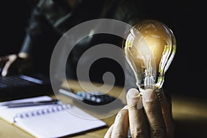 Business man holding light bulb on the desk in office and using  computer in  financial,accounting,energy,idea concept