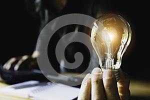 Business man holding light bulb on the desk in office and using  computer in  financial,accounting,energy,idea concept
