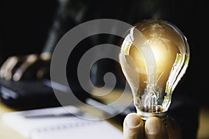 Business man holding light bulb on the desk in office and using  computer in  financial,accounting,energy,idea concept