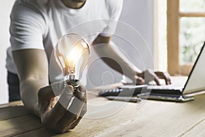 Business man holding light bulb on the desk in office and using  computer in  financial,accounting,energy,idea concept