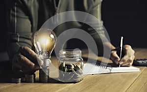 Business man holding light bulb on the desk in office and writing on note book it for financial,accounting,energy,idea concept