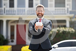 Business Man holding piggy bank on rich house background. Save money and financial investment.