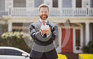 Business Man holding piggy bank on rich house background. Save money and financial investment.