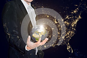 Business man holding the small world in his hands against america city night light.Save our planet earth ecology concept.