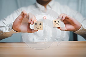 Business man holding a wooden cube Happy and angry icons compare service feedback and satisfaction ratings.