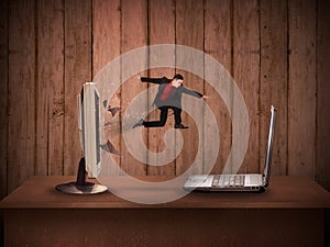 Business man jumping from desktop computer to laptop