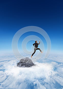 Business man jumping off mountain peak in the clouds