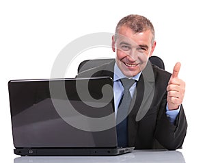 Business man at laptop, shows thumb up sign