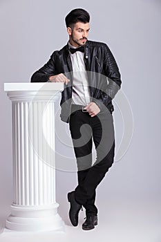 Business man leaning on a white column while looking down.