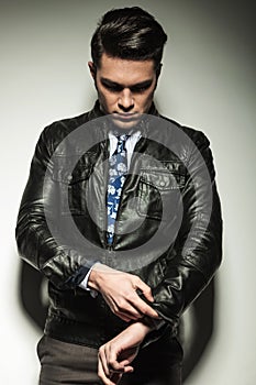 Business man in leather jacket, looking down while fixing his sleeve.