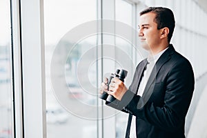 Business man looking with binoculars on competitors over panoramic windows